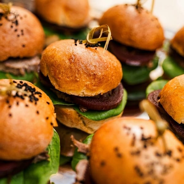 Close-up of several mini sliders with dark buns, green lettuce, and black sesame seeds.