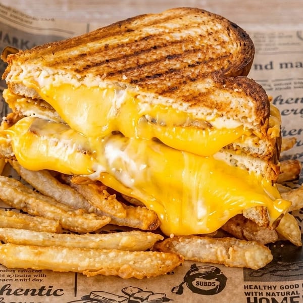 Grilled cheese sandwich with melted cheese and a side of fries on newspaper-patterned paper.