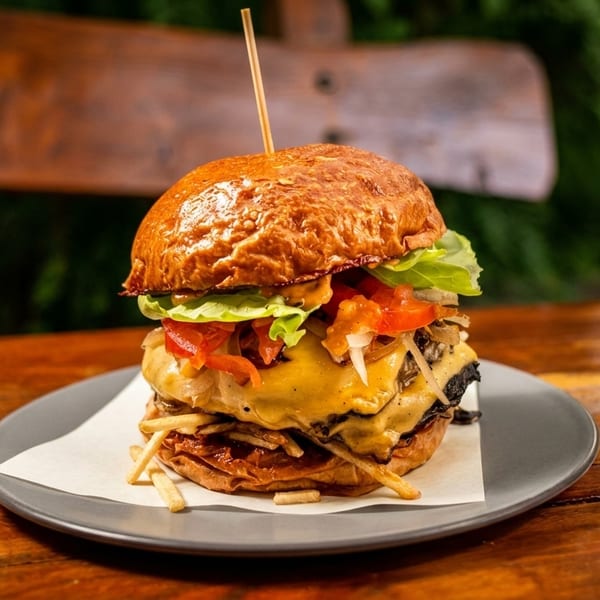 Gourmet burger with melted cheese, lettuce, tomatoes, and fries on a plate.